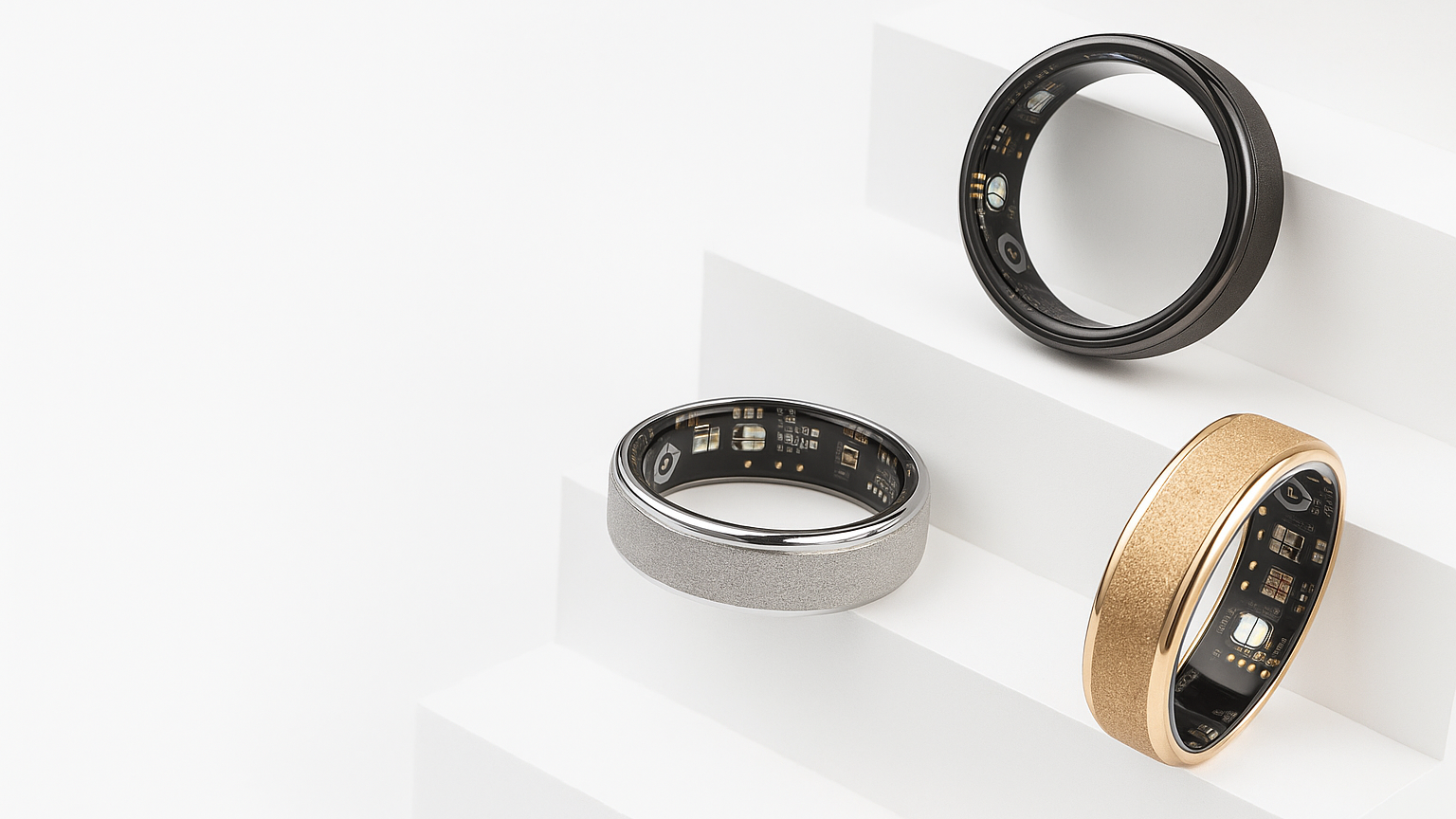 Three smart rings in black, silver, and gold on a white background